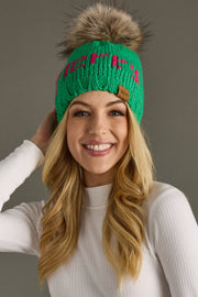 Woman wearing a green knit beanie with a fur pom-pom against a gray background