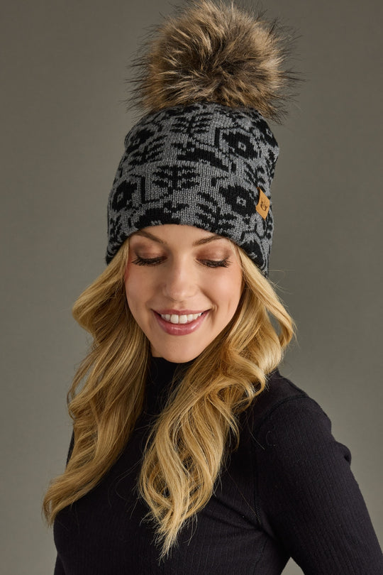 Woman wearing a patterned beanie with a pom-pom on a gray background