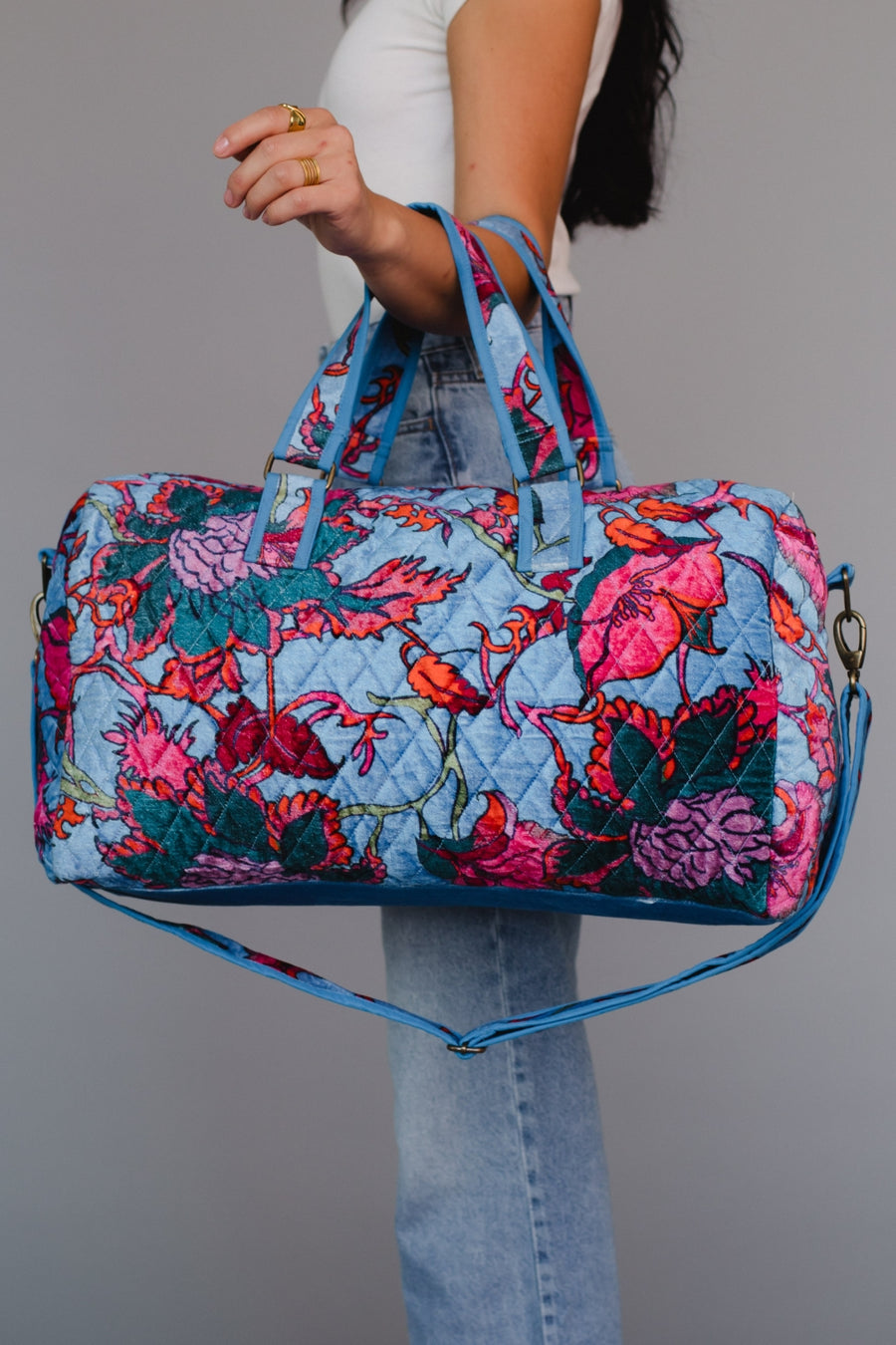 Person holding a colorful floral-patterned duffel bag against a gray background