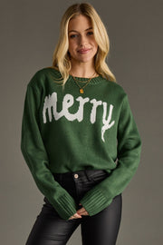 Woman wearing a green sweater with 'merry' text on a gray background