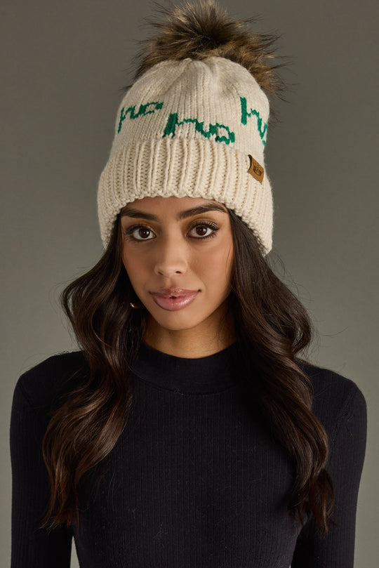 Woman wearing a cream beanie with text and a logo on a gray background
