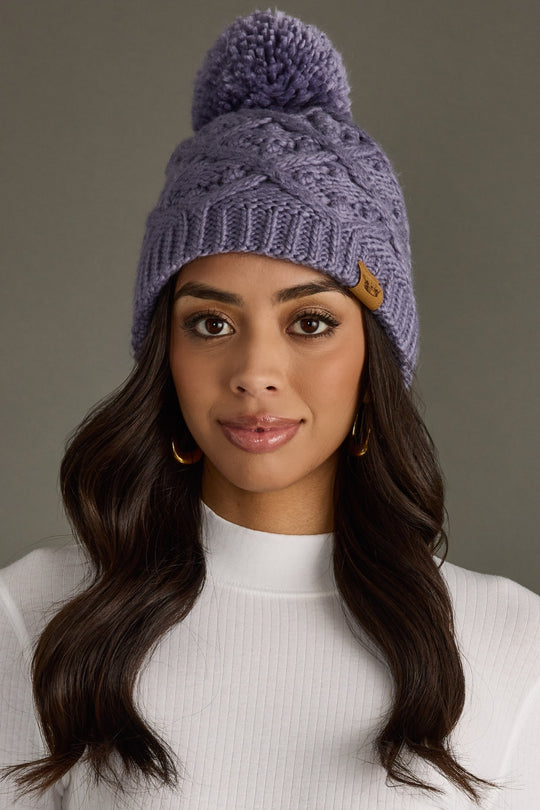 Woman wearing a purple knit beanie with a pom-pom on a gray background