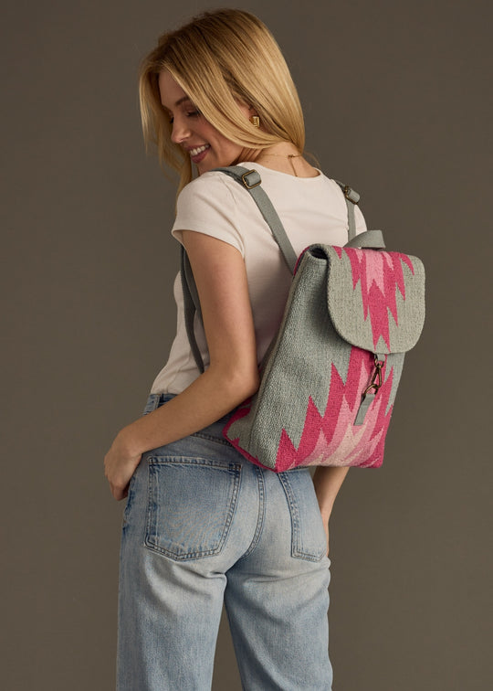 Woman wearing a gray and pink patterned backpack against a brown background