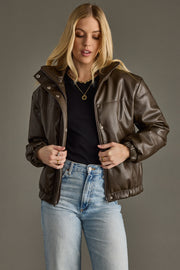 Woman wearing a brown leather jacket over a black top and blue jeans on a gray background