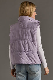 Person wearing a purple puffer vest and blue jeans on a gray background