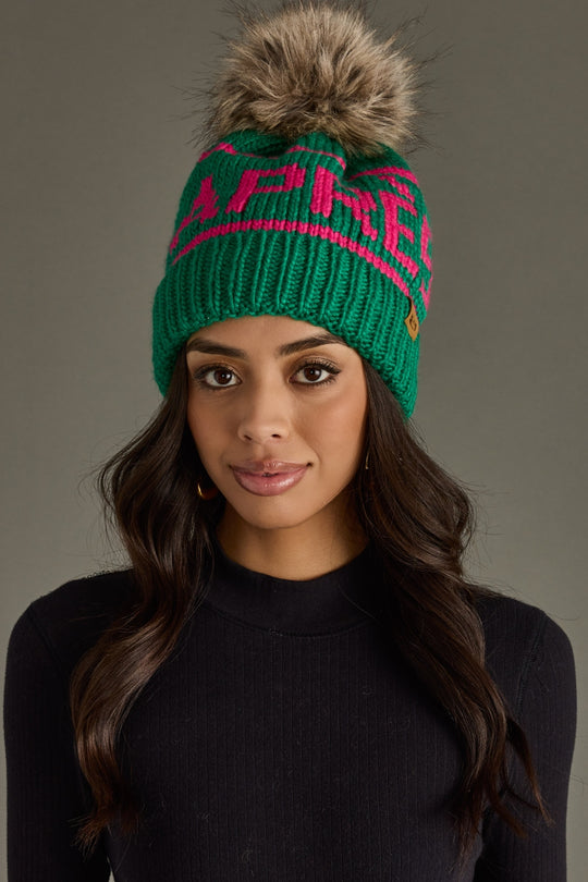 Woman wearing a green beanie with pink text against a gray background
