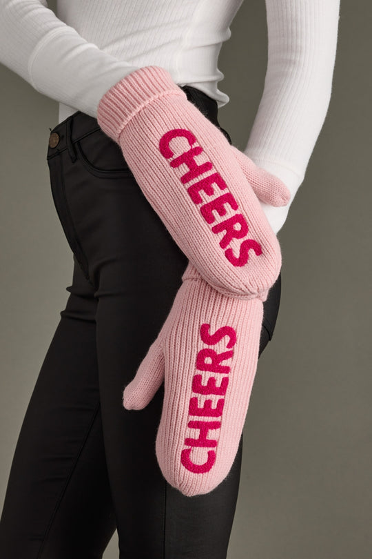 Pink mittens with 'CHEERS' text worn by a person against a neutral background
