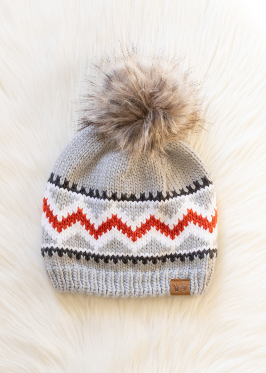 Knitted beanie with a fur pom-pom on a light background