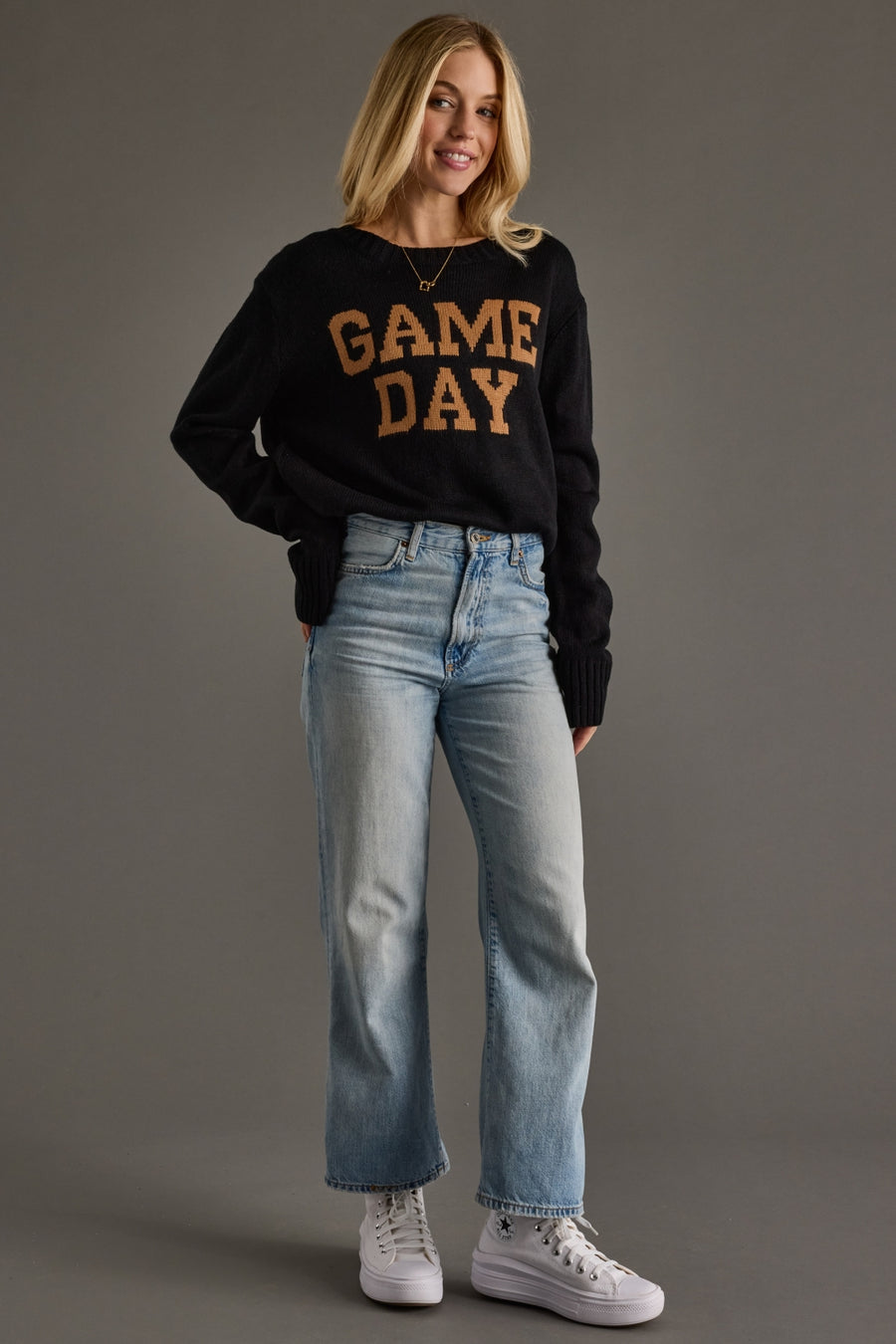 Woman wearing a black 'GAME DAY' sweater and blue jeans on a gray background