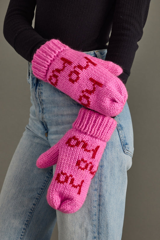 Person wearing pink mittens with text, standing against a neutral background