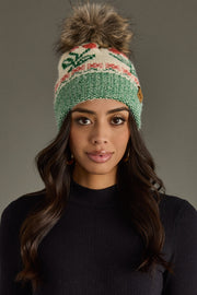 Woman wearing a green knitted beanie with a pom-pom against a gray background