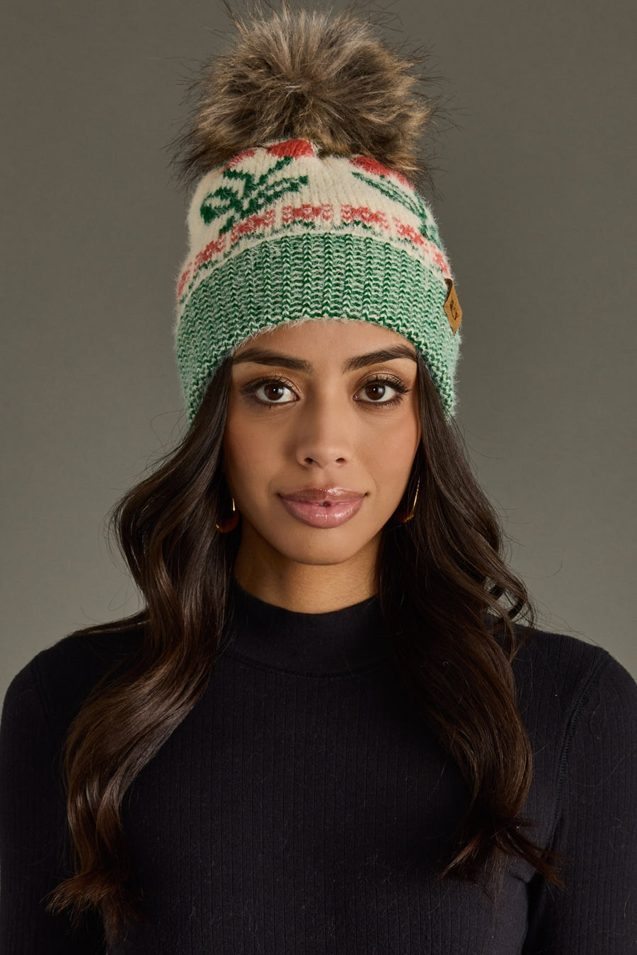 Woman wearing a green knitted beanie with a pom-pom against a gray background