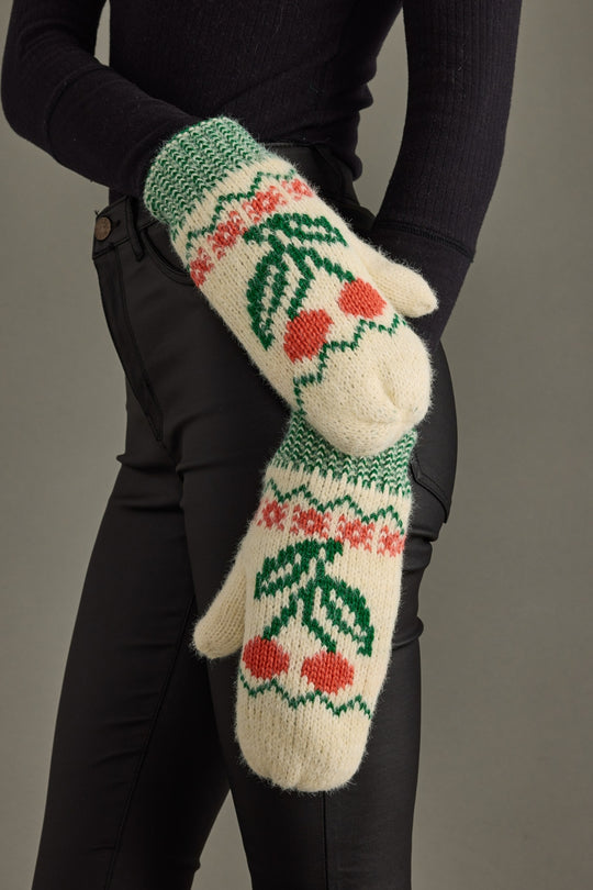 Knitted mittens with cherry pattern worn by a person against a neutral background