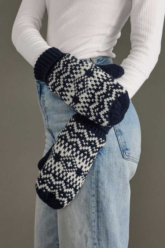 Person wearing dark navy and white patterned mittens with a plain background