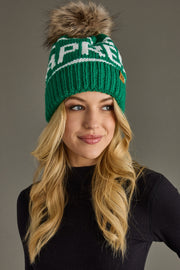 Woman wearing a green knit beanie with a fur pom-pom on a gray background