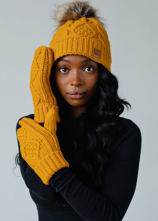 Woman wearing a mustard yellow knit hat and gloves against a gray background