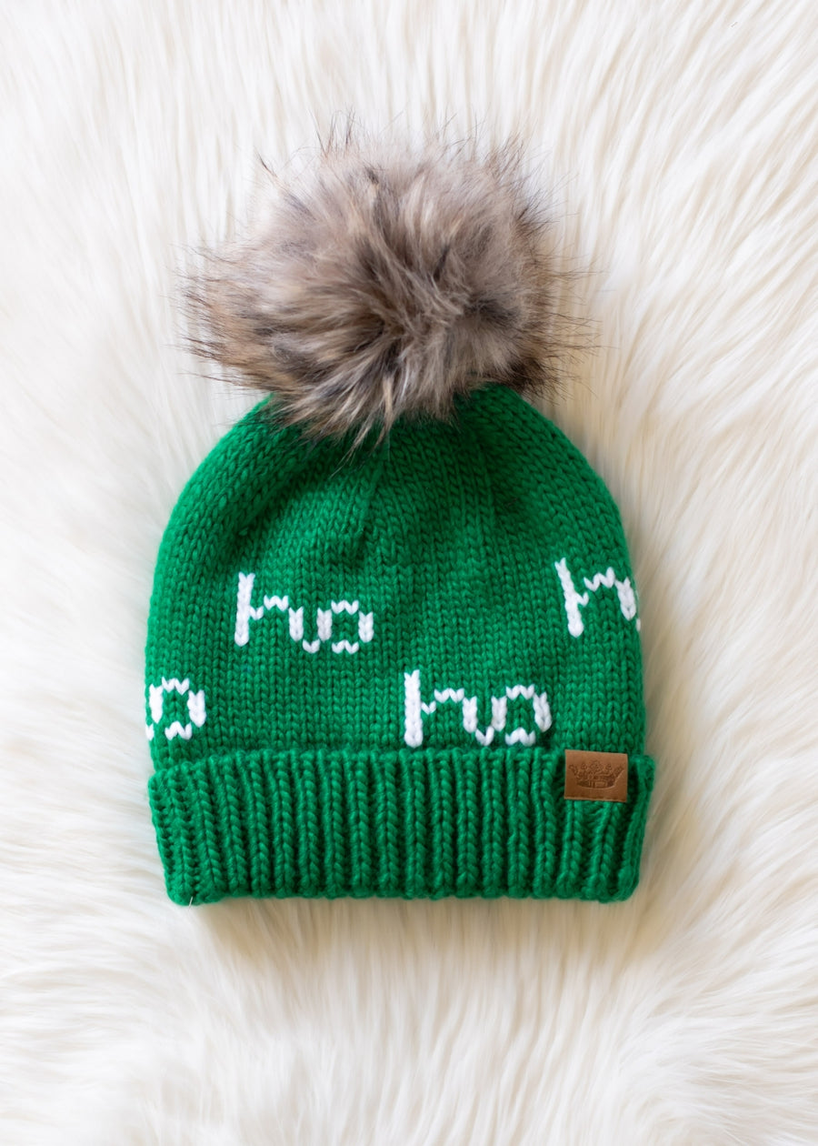 Green knit hat with fur pom-pom on a white fluffy surface