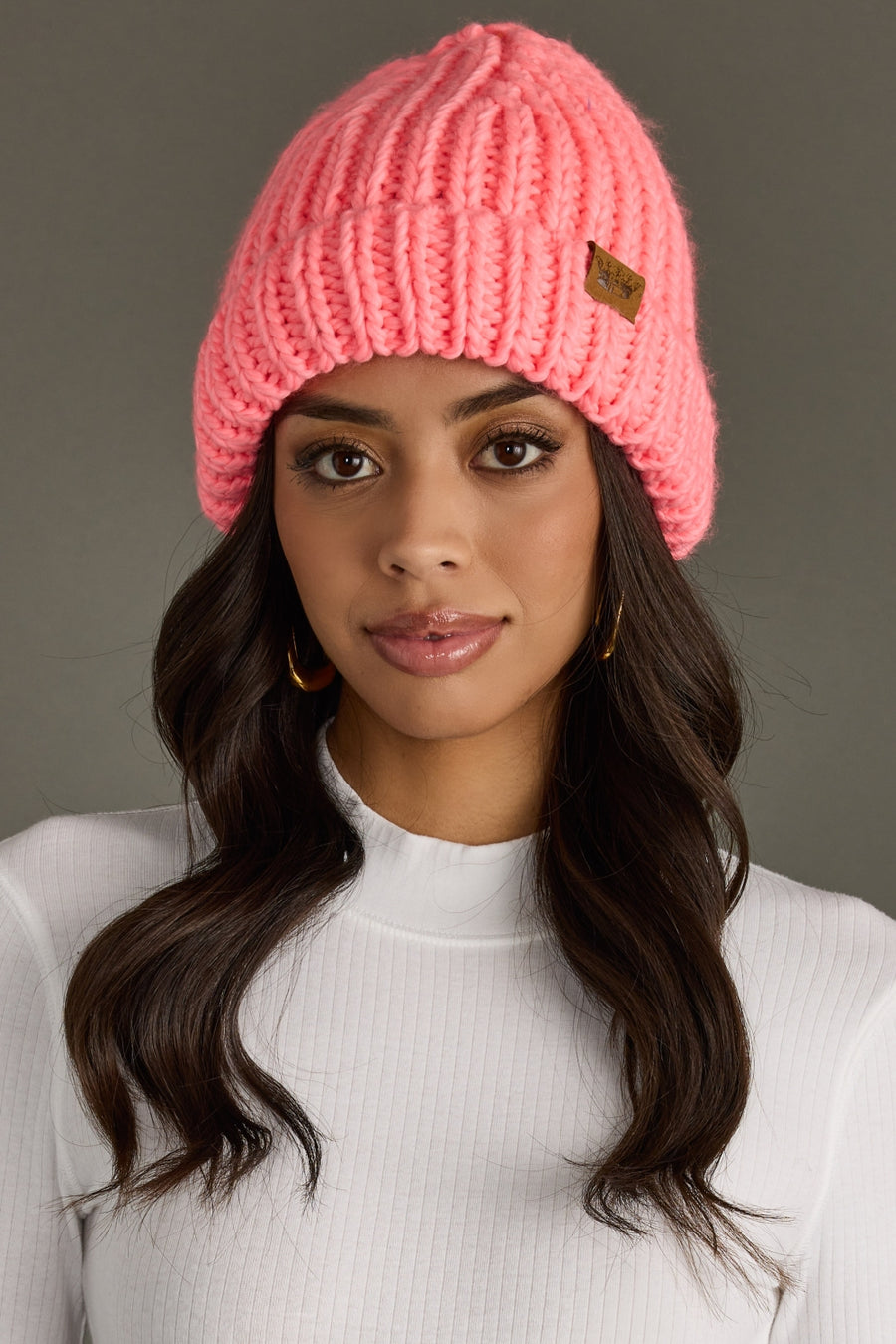 Woman wearing a pink knit beanie with a brand logo against a gray background