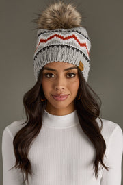 Woman wearing a gray knit beanie with a pom-pom on a plain background