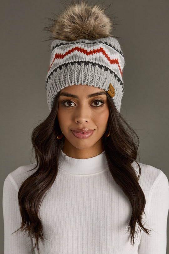 Woman wearing a gray knit beanie with a pom-pom on a plain background