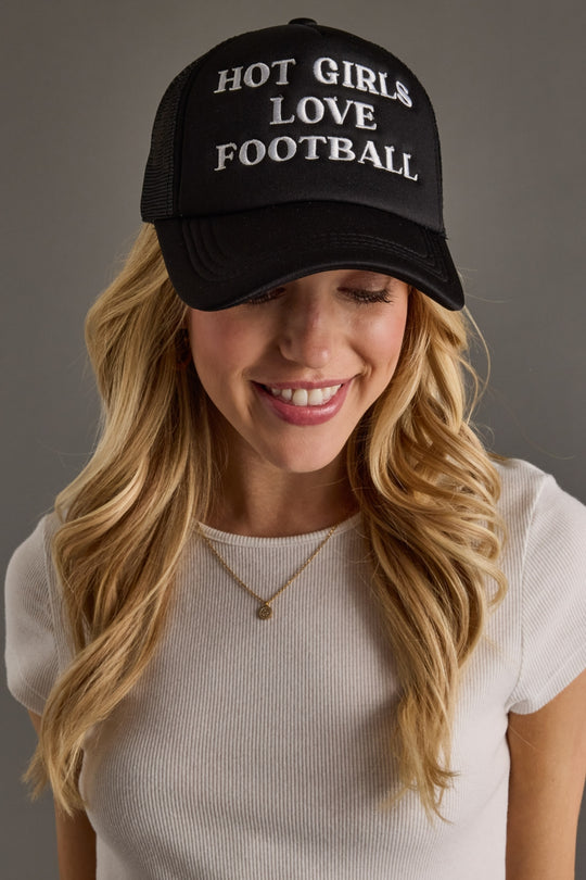 Woman wearing a black cap with 'HOT GIRLS LOVE FOOTBALL' text on a gray background