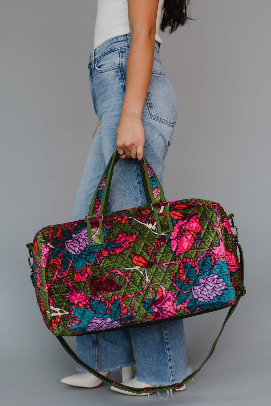 Person holding a colorful floral-patterned duffel bag against a neutral background