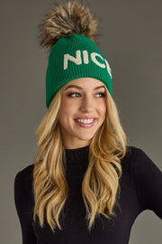 Person wearing a green beanie with 'NICE' text and a fluffy pom-pom on a gray background