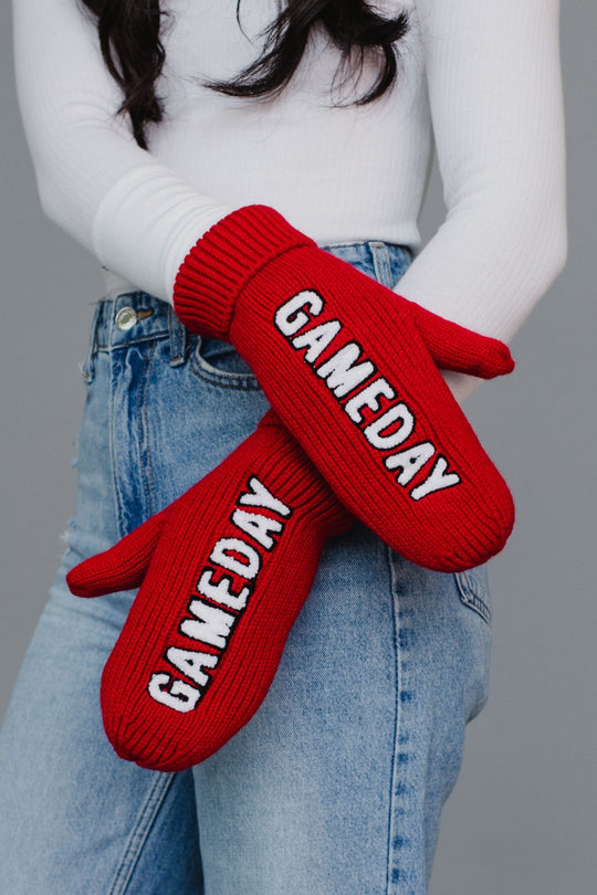Red 'GAMEDAY' mittens worn by a person against a gray background