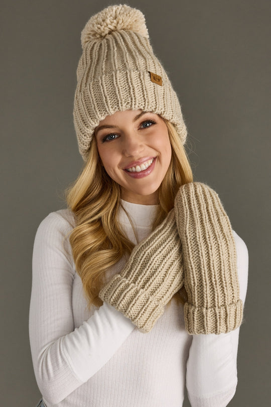 Woman wearing a beige knit hat and mittens against a gray background