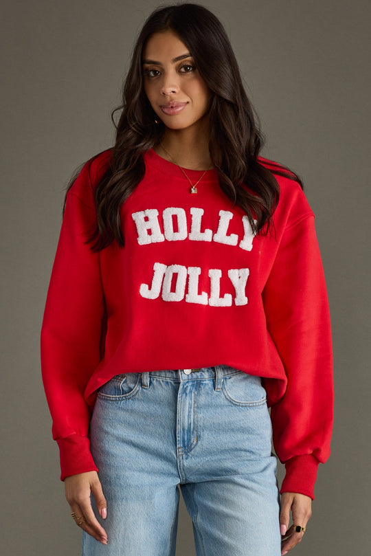 Person wearing a red 'Holly Jolly' sweater with blue jeans on a gray background