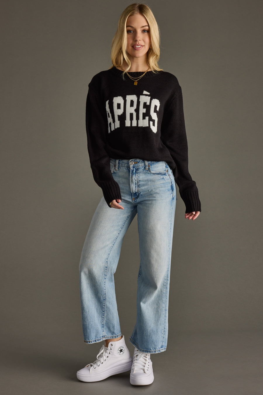Woman wearing a black sweater with 'APRèS' text and light blue jeans on a gray background