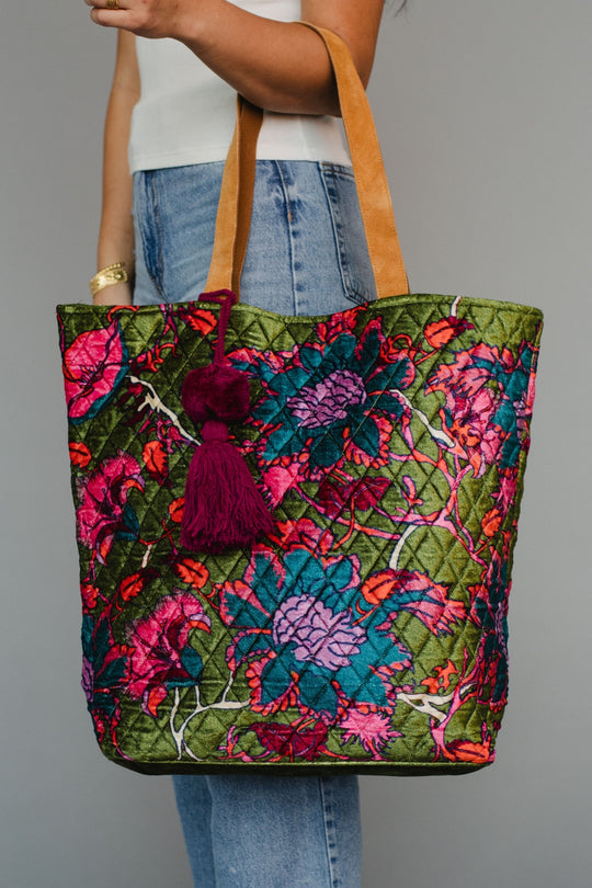 Colorful floral-patterned tote bag with a tassel held by a person wearing jeans.