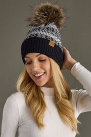 Woman wearing a dark navy and white patterned beanie with a pom-pom, against a neutral background