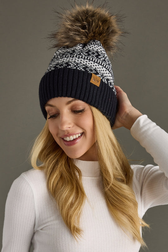 Woman wearing a dark navy and white patterned beanie with a pom-pom, against a neutral background
