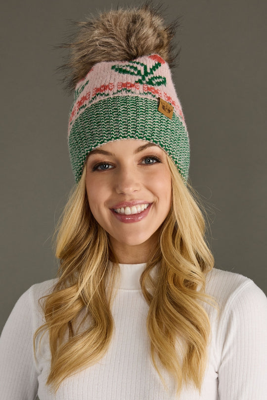 Woman wearing a green knitted beanie with a pom-pom against a brown background