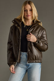 Woman wearing a brown leather jacket and blue jeans against a gray background