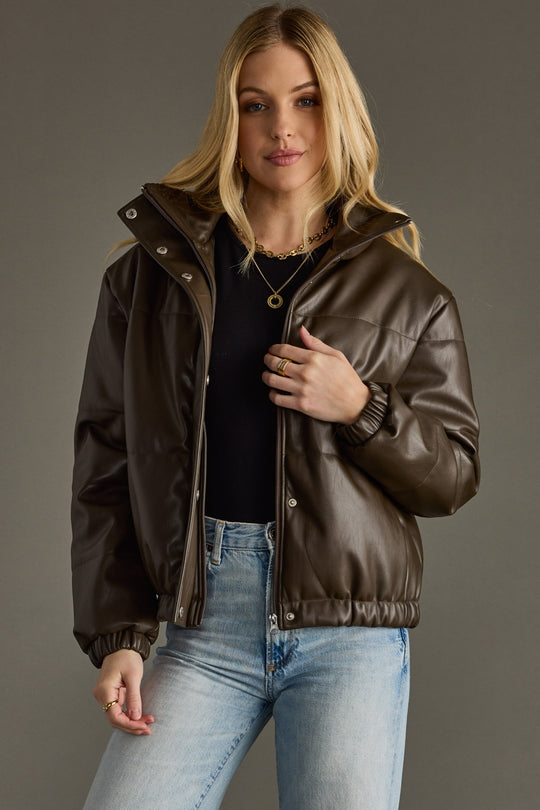 Woman wearing a brown leather jacket and blue jeans against a gray background