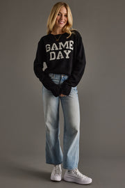 Person wearing a black 'GAME DAY' sweater and light blue jeans on a gray background