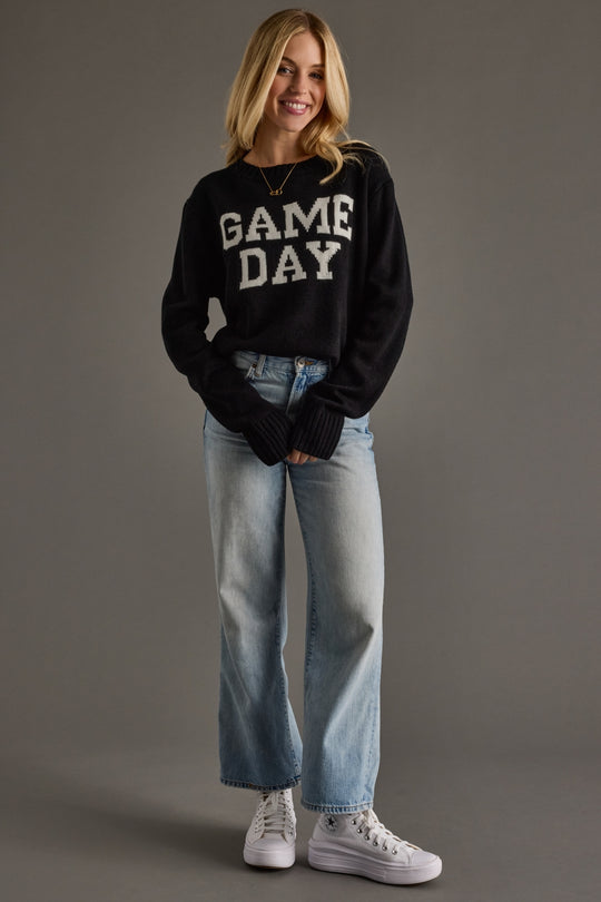 Person wearing a black 'GAME DAY' sweater and light blue jeans on a gray background