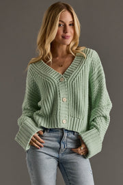 Woman wearing a light green knitted cardigan and blue jeans against a gray background