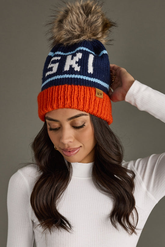 Woman wearing a colorful knit beanie with 'Ski' text against a neutral background