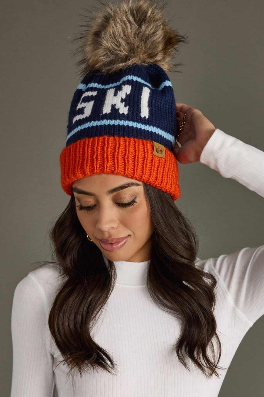 Woman wearing a colorful knit beanie with 'Ski' text against a neutral background