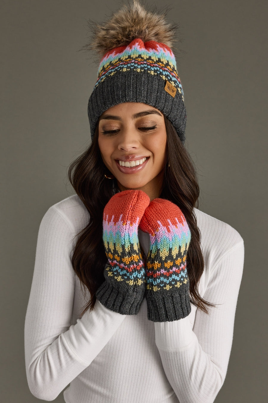 Woman wearing a colorful knit beanie and mittens against a gray background