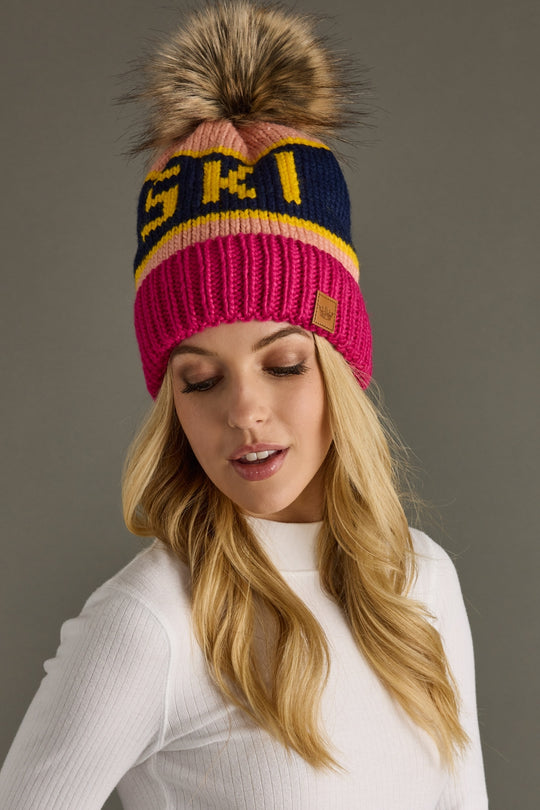 Woman wearing a colorful knit beanie with a pom-pom on a gray background