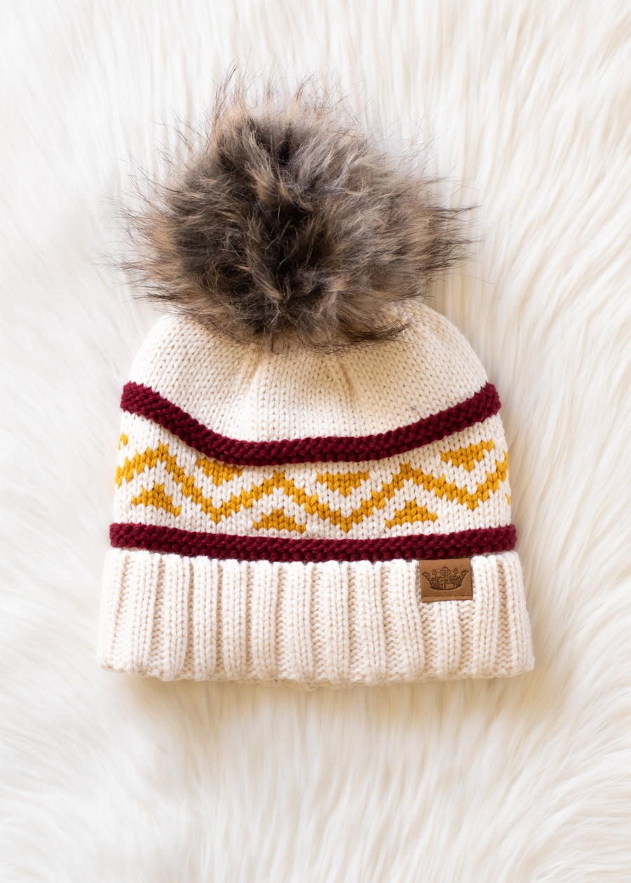 Knitted beanie with a fur pom-pom on a white textured background