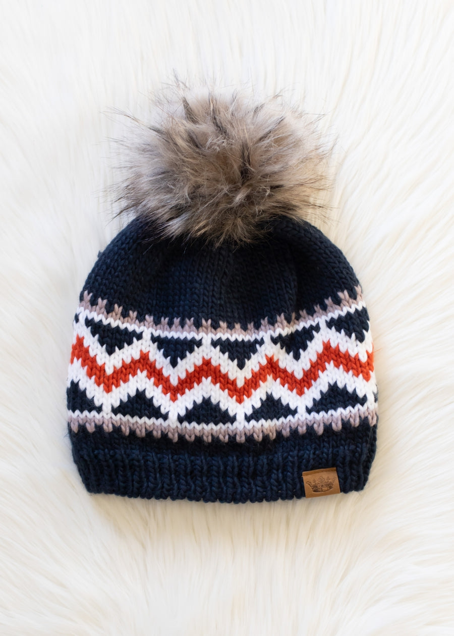 Knitted beanie with a patterned design and fur pom-pom on a white background
