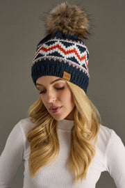 Woman wearing a patterned knit hat with a fur pom-pom against a gray background