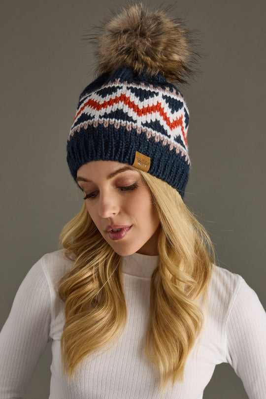 Woman wearing a patterned knit hat with a fur pom-pom against a gray background