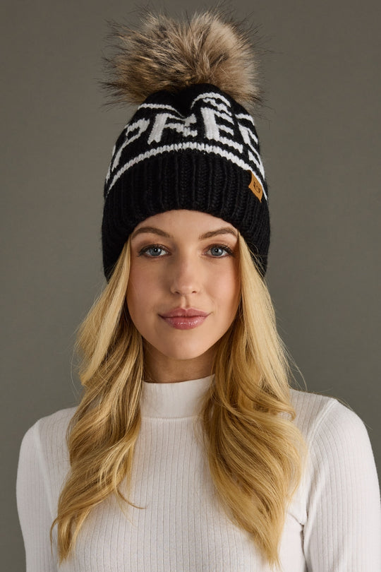 Woman wearing a black knit beanie with a fur pom-pom on a gray background