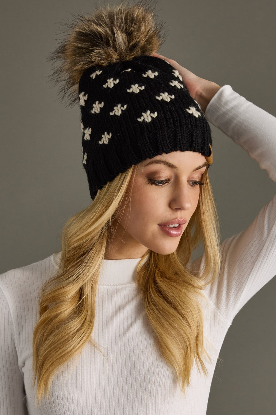 Woman wearing a black beanie with a fur pom-pom against a gray background